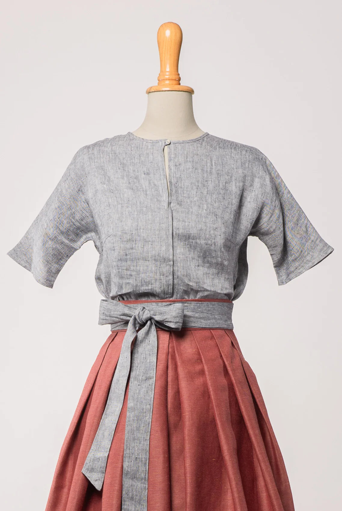 Bluse Romy aus blaugrauem Bio-Leinen, kombiniert mit Trachtenrock Charlie und farblich abgestimmtem Schürzenband – Frontansicht auf Büste, handgefertigt in München von Zirbenfux