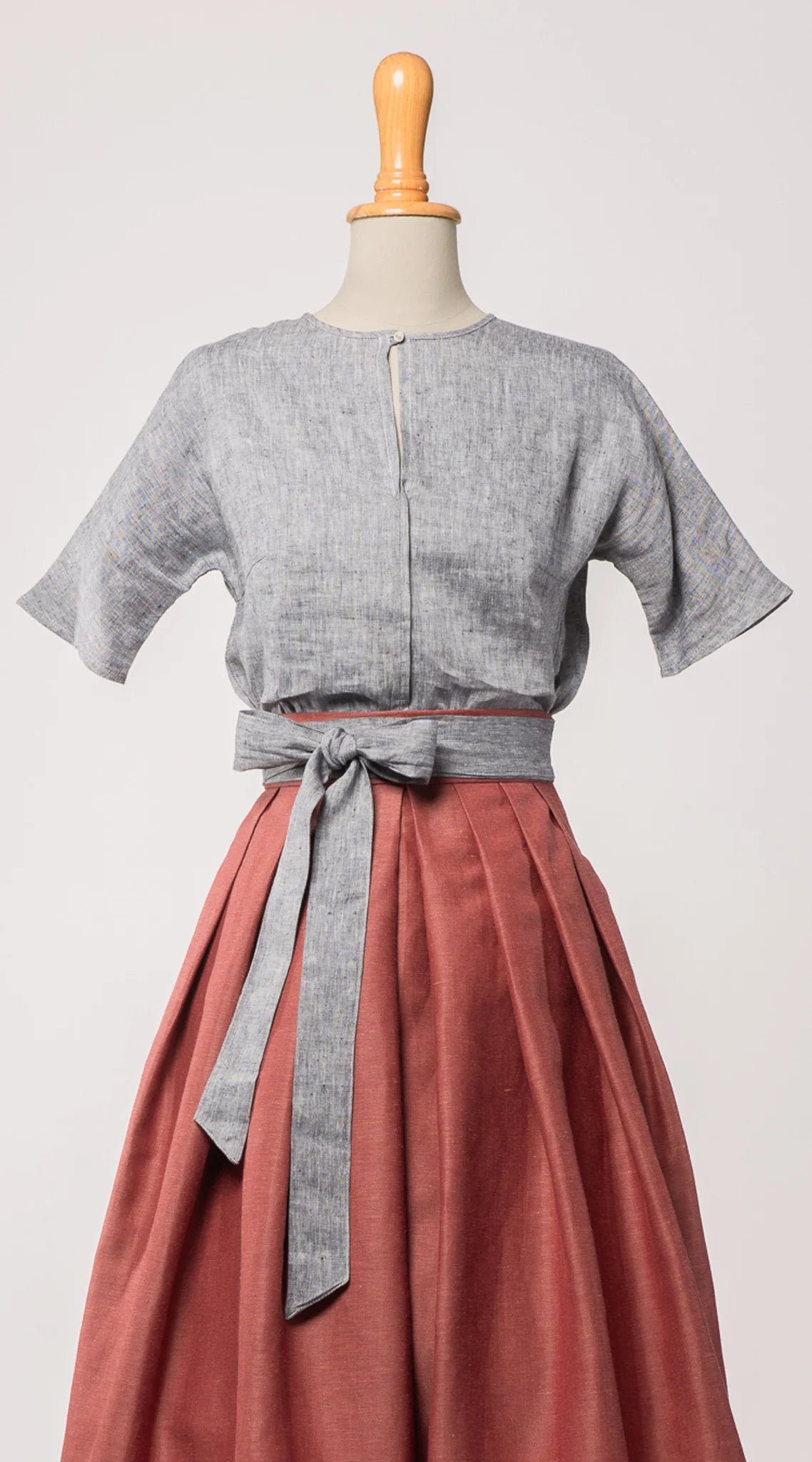 Bluse Romy aus blaugrauem Bio-Leinen, kombiniert mit Trachtenrock Charlie und farblich abgestimmtem Schürzenband – Frontansicht auf Büste, handgefertigt in München von Zirbenfux