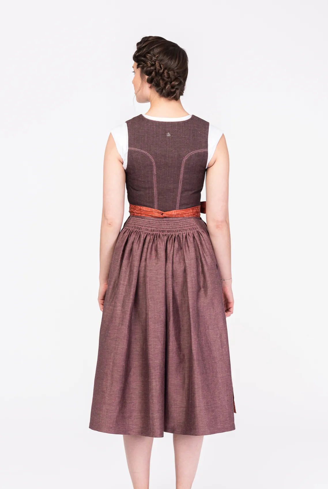 Dirndl Ava aus Leinen in Malve mit Schürze in Terrakotta – Rückansicht am Model, handgefertigt in München von Zirbenfux