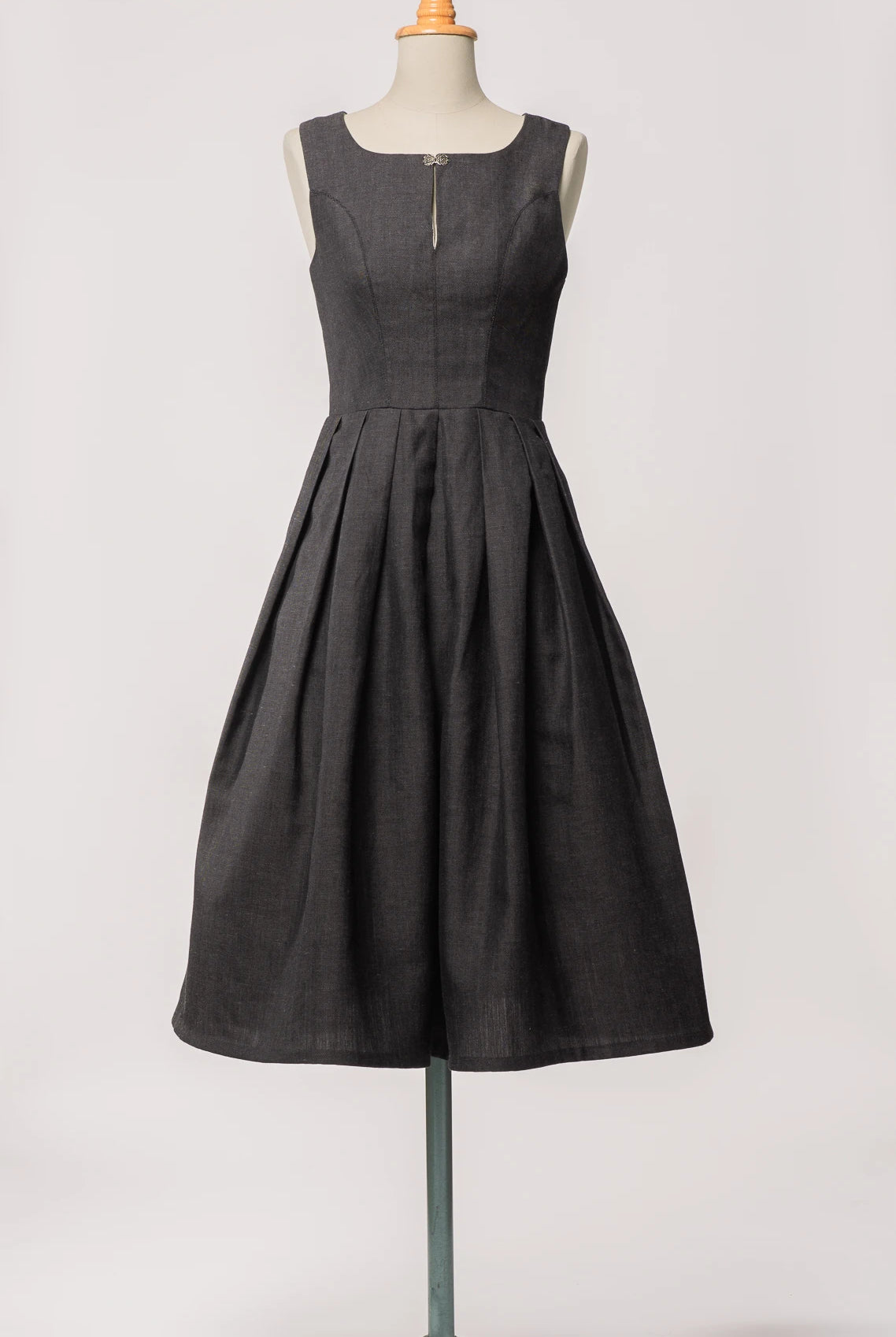 Hochgeschlossenes Dirndl Wanda von Zirbenfux in Anthrazit aus regional gewebtem Leinen-Wolle-Mix, mit filigraner Schließe und in Falten gelegtem Rock, an einer Schneiderbüste.