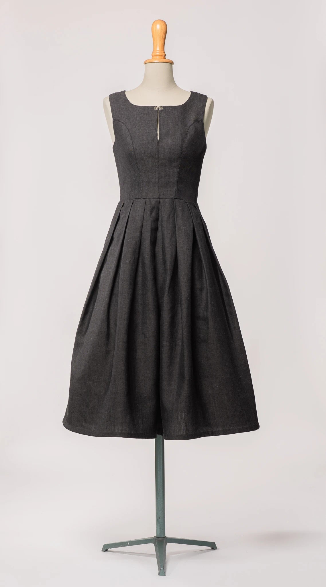 Hochgeschlossenes Dirndl Wanda von Zirbenfux in Anthrazit aus regional gewebtem Leinen-Wolle-Mix, mit filigraner Schließe und in Falten gelegtem Rock, an einer Schneiderbüste.