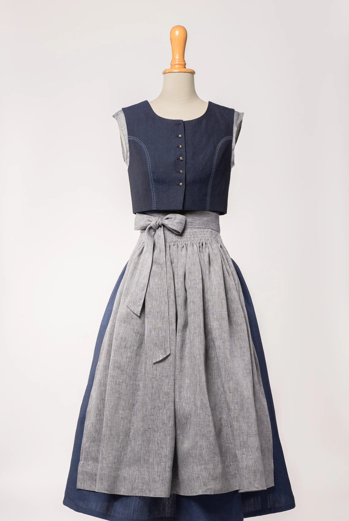 Dirndlschürze aus blaugrauem Bio-Leinen – Frontansicht auf Büste, kombiniert mit dunkelblauem Dirndl, nachhaltig gefertigt von Zirbenfux