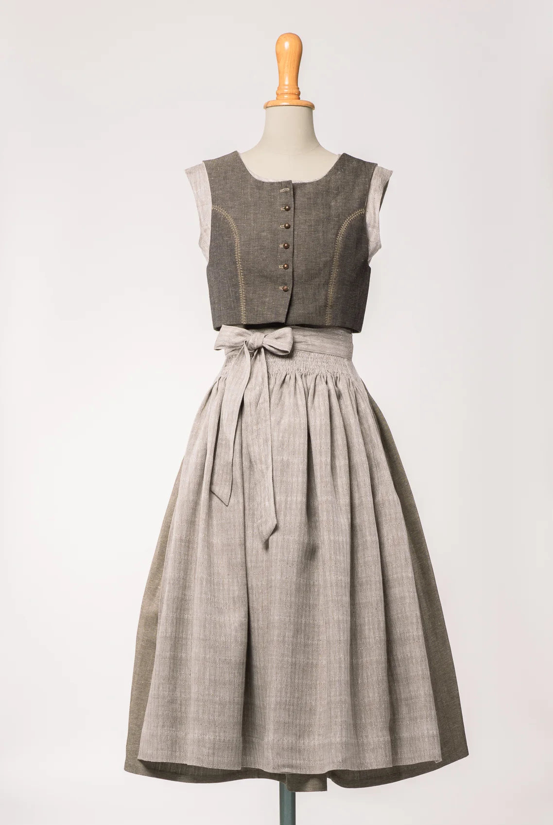 Dirndlschürze aus naturfarbenem Bio-Leinen mit eingewebtem Muster, kombiniert mit goldbraunem Fuxerl und Rock– Frontansicht auf Büste, handgefertigt in München von Zirbenfux