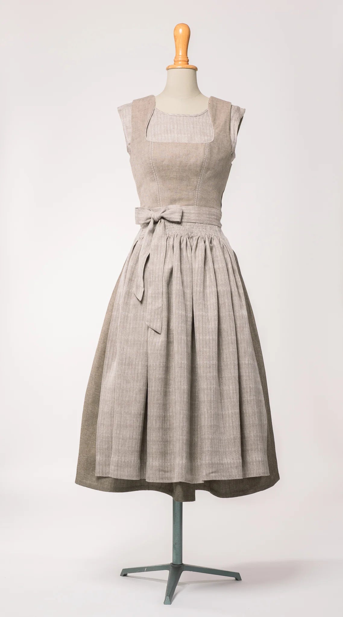 Dirndlschürze aus naturfarbenem Bio-Leinen mit eingewebtem Muster, kombiniert mit Mieder Ava in hellem Naturton und Rock Marlene in goldbraun – Frontansicht auf Büste, handgefertigt von Zirbenfux