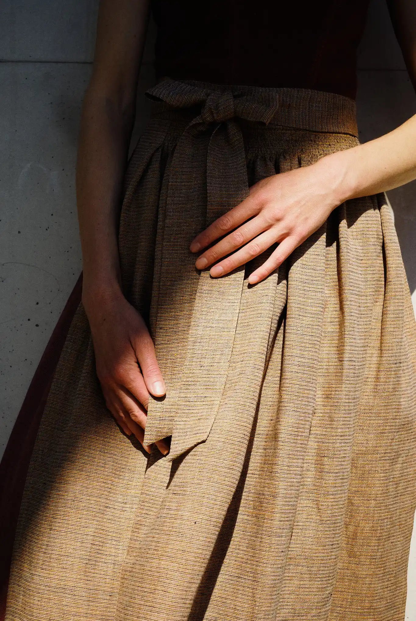 Dirndlschürze in Ocker mit Streifen aus Leinen, Nahaufnahme der Schürze am Model mit ausgeprägtem Licht- und Schattenspiel, reduziert inszeniert von Zirbenfux.
