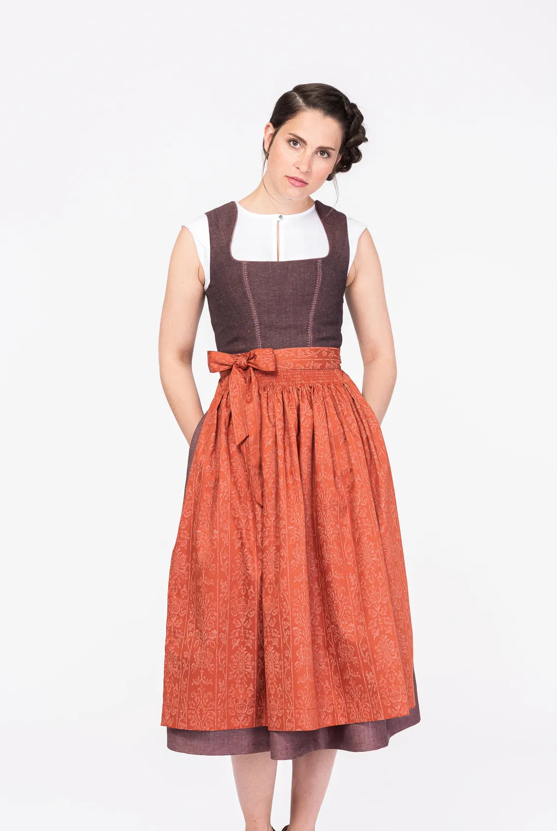 Dirndlschürze aus Baumwolle in Orange-Terrakotta – Frontansicht am Model, kombiniert mit Dirndl in Beerentönen, handgefertigt in München von Zirbenfux