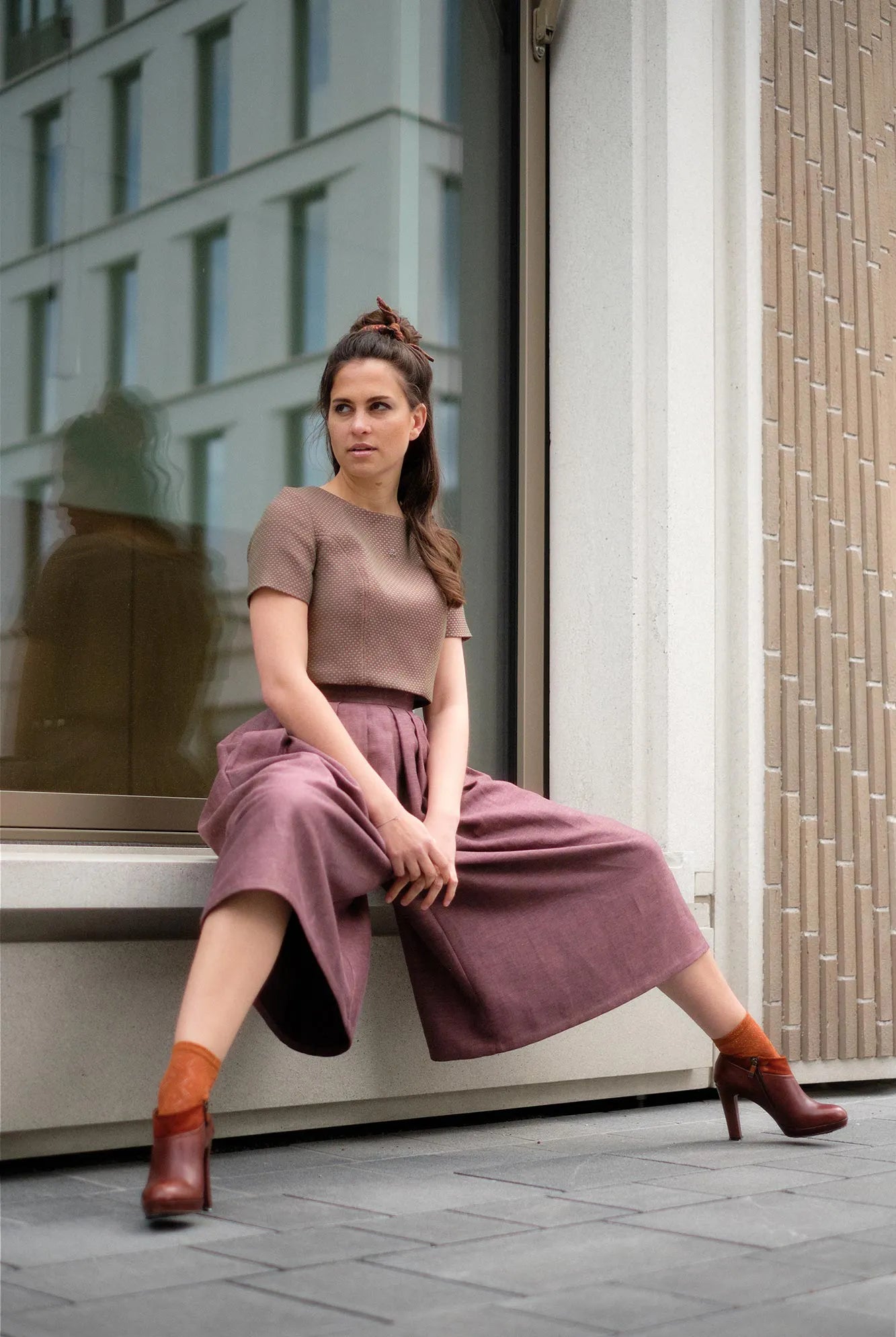 Hosenrock Audrey mit Fuxerl TILDA im Set in Malve aus Leinen, Model sitzend auf niedrigem Fenstervorsprung vor moderner urbaner Häuserfassade, Hosenrock stimmungsvoll in Szene gesetzt, klar interpretiert von Zirbenfux.