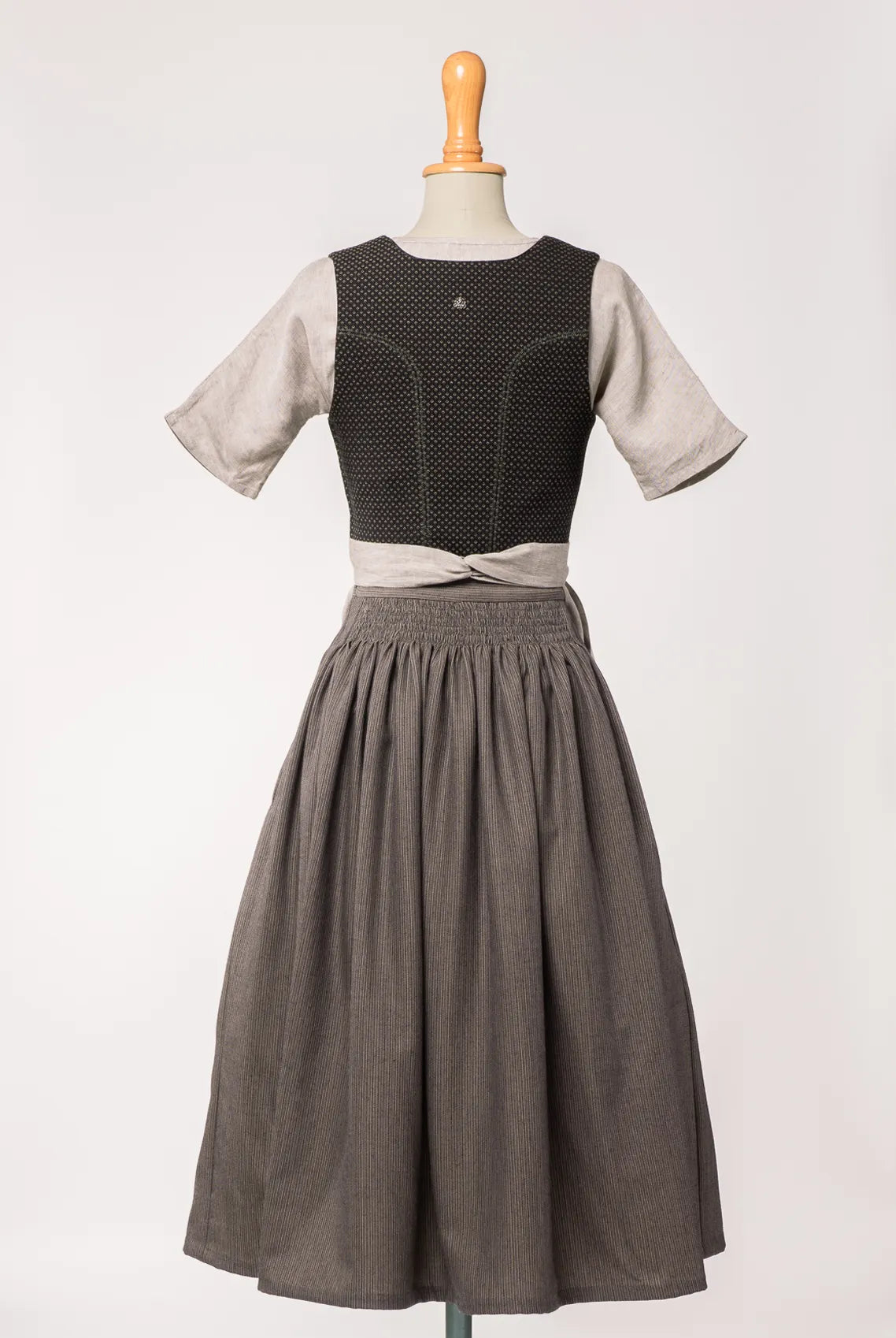 Mieder Ava aus schwarzer Schurwolle mit Webmuster, kombiniert mit Rock Marlene und naturfarbener Leinenschürze – Rückansicht auf Büste, handgefertigt von Zirbenfux