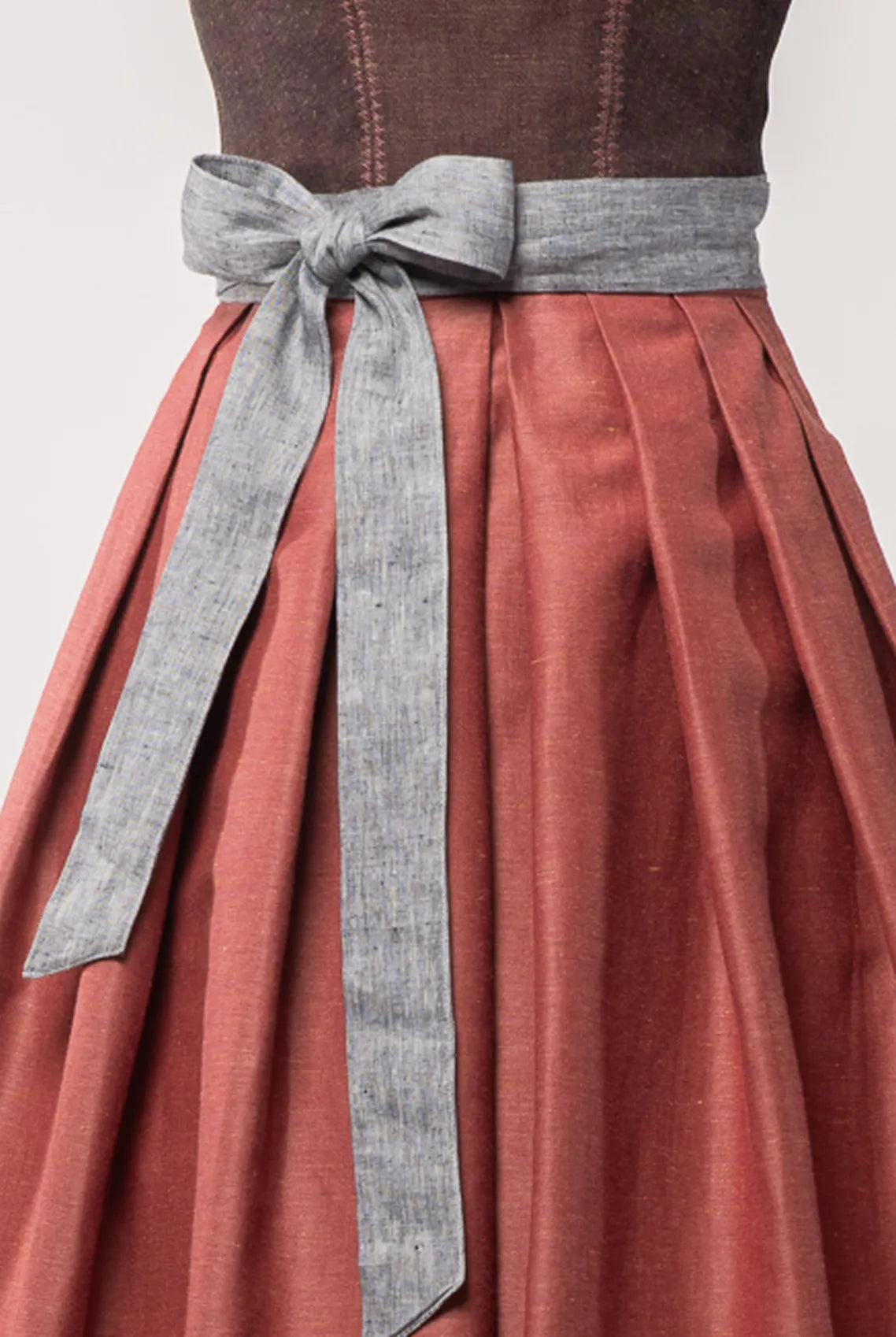 Nahaufnahme des Schürzenbands aus blaugrauem Bio-Leinen, kombiniert mit Trachtenrock Charlie in pinker Beere – Detailansicht auf Büste, moderne Tracht von Zirbenfux