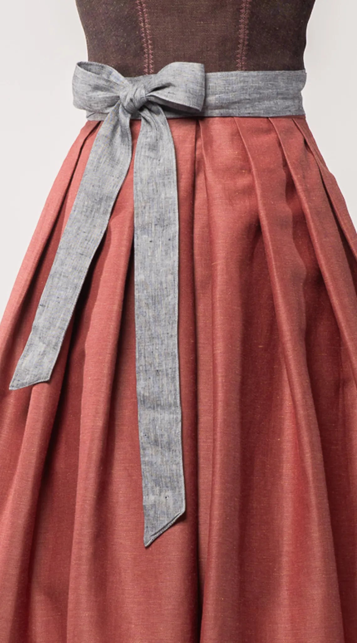 Nahaufnahme des Schürzenbands aus blaugrauem Bio-Leinen, kombiniert mit Trachtenrock Charlie in pinker Beere – Detailansicht auf Büste, moderne Tracht von Zirbenfux