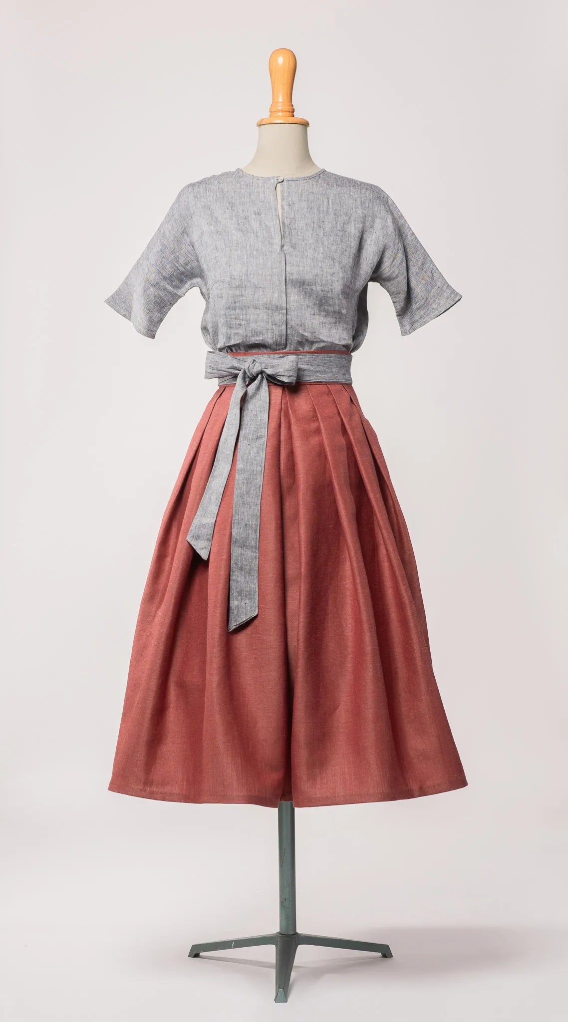 Schürzenband aus blaugrauem Bio-Leinen – Frontansicht auf Büste, kombiniert mit gleichfarbiger Bluse und Rock in pinker Beere, nachhaltig gefertigt von Zirbenfux