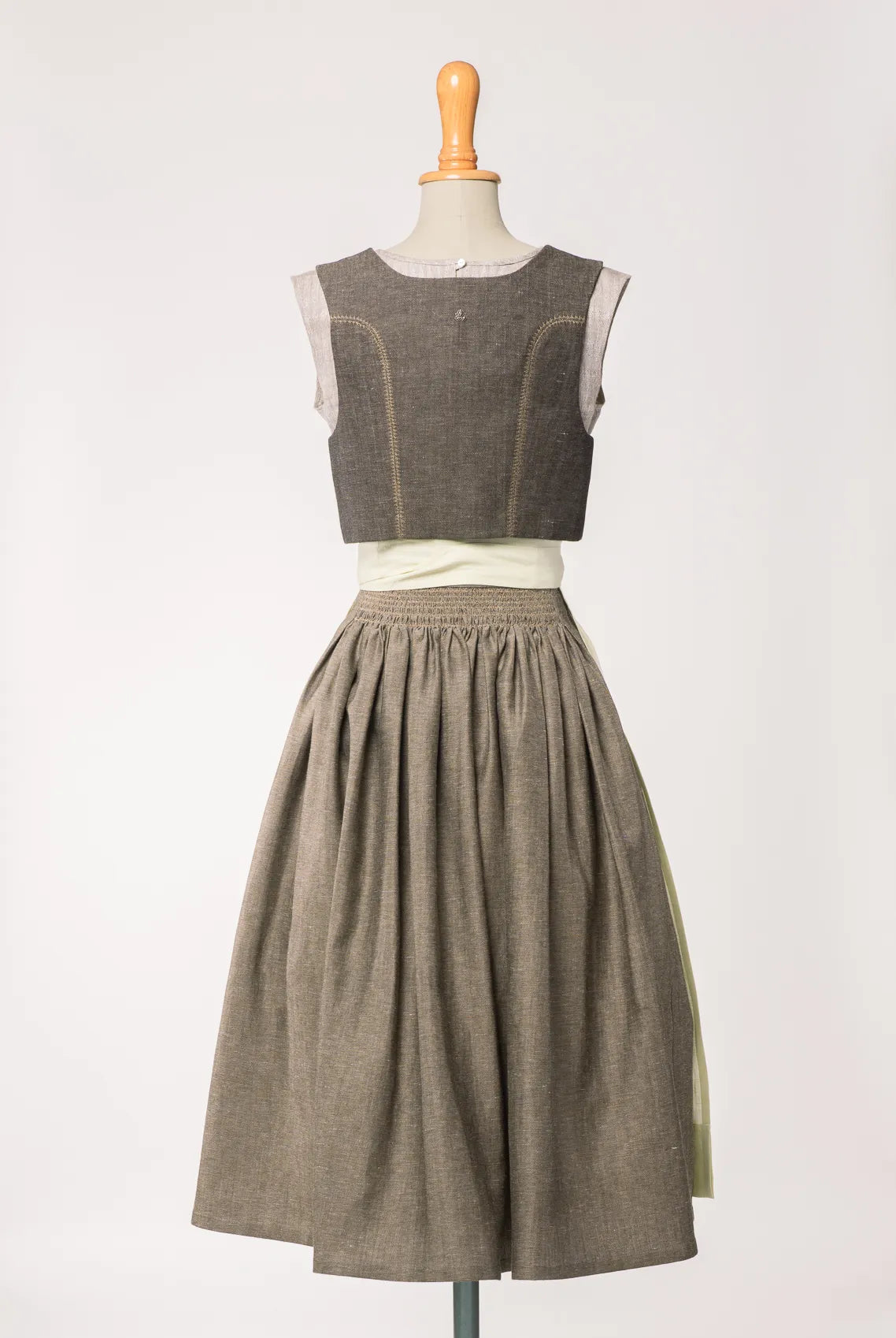 Trachtenrock Marlene aus gold-naturfarbener Leinen-Schurwolle-Mischung, kombiniert mit Fuxerl Charlie und Schürze – Rückansicht auf Büste, zeitlos interpretiert von Zirbenfux