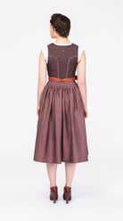 Dirndl Ava aus Leinen in Malve mit Schürze in Terrakotta – Rückansicht am Model, handgefertigt in München von Zirbenfux