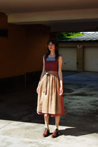 Model trägt Dirndl Ava in pinker Beere mit ocker-gestreifter Schürze – steht regungslos in einer Garageneinfahrt, halb im Schatten, halb in der Sonne, urban-minimalistisch inszeniert von Zirbenfux