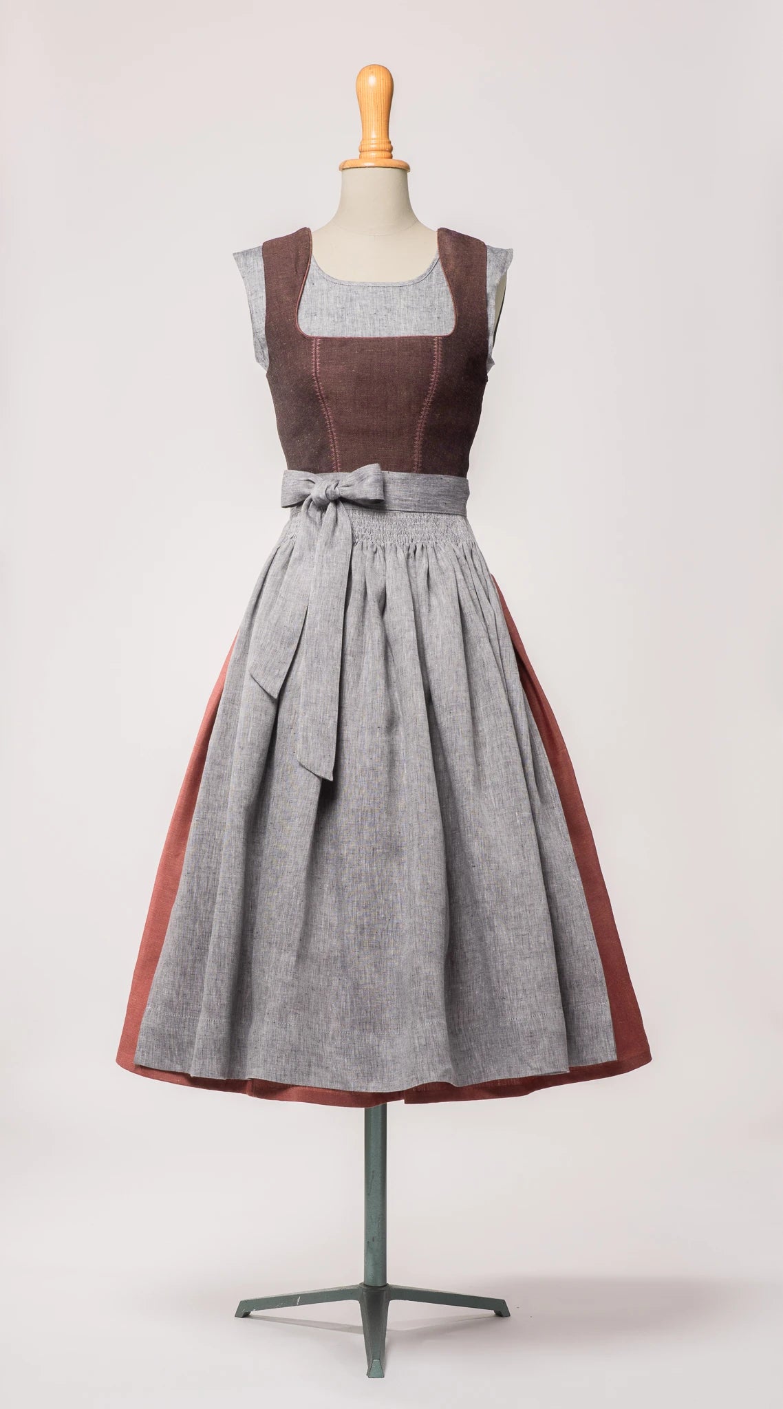 Dirndlschürze aus blaugrauem Bio-Leinen – Frontansicht auf Büste, kombiniert mit Dirndl in Beerenfarben, nachhaltig gefertigt von Zirbenfux