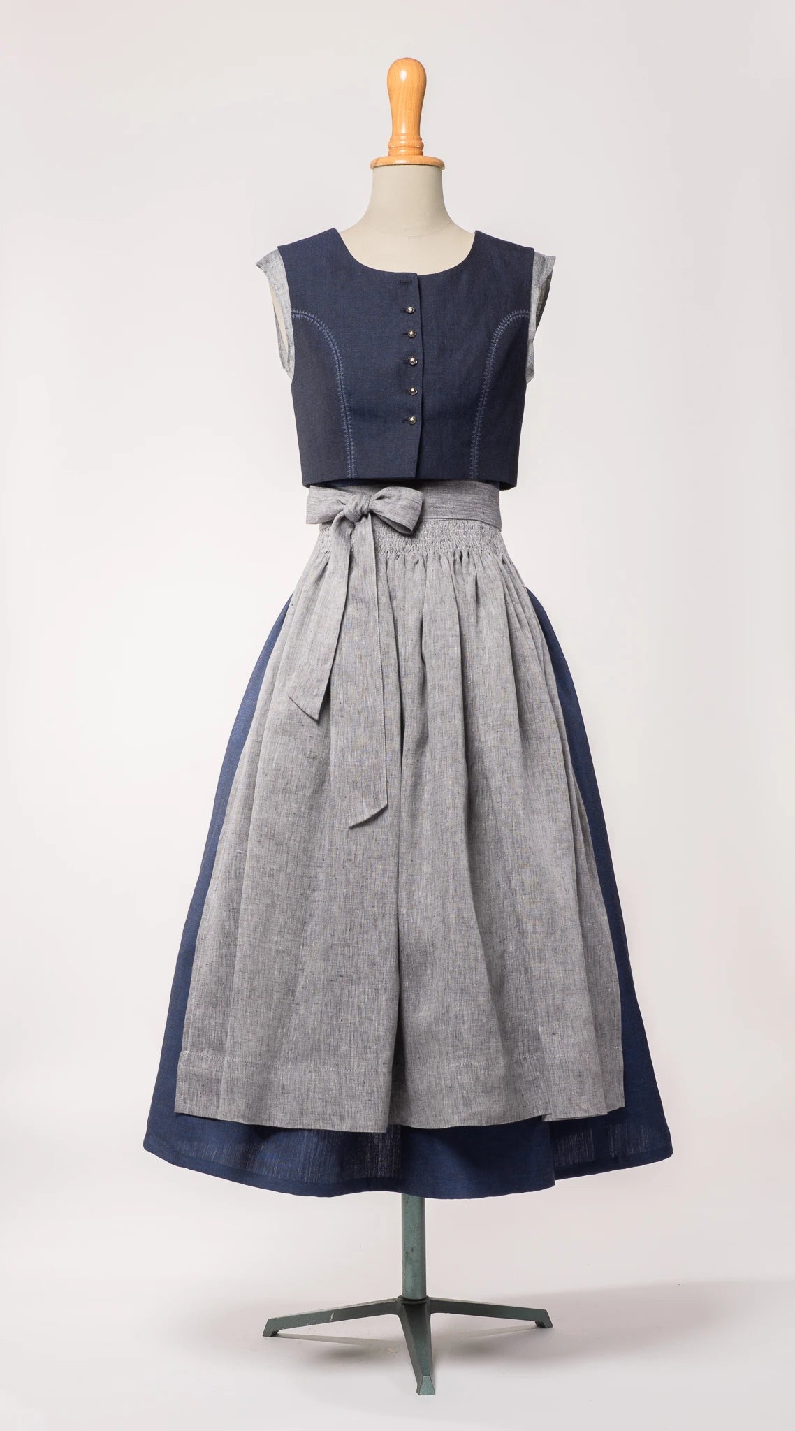 Dirndlschürze aus blaugrauem Bio-Leinen – Frontansicht auf Büste, kombiniert mit dunkelblauem Dirndl, nachhaltig gefertigt von Zirbenfux