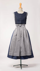 Dirndlschürze aus blaugrauem Bio-Leinen – Frontansicht auf Büste, kombiniert mit dunkelblauem Dirndl, nachhaltig gefertigt von Zirbenfux