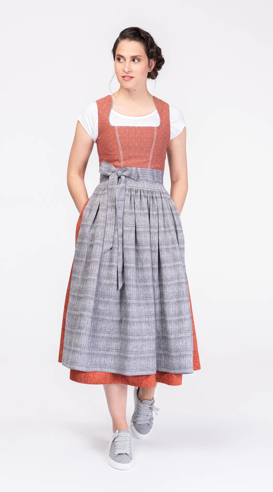 Dirndlschürze aus blaugrauem Bio-Leinen mit eingewebtem Muster – Frontansicht am Model mit Dinrdl in Terrakotta-Farben, nachhaltig gefertigt von Zirbenfux