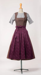 Dirndlschürze aus brombeerfarbener Baumwolle mit Blumenrankenmuster – Frontansicht auf Büste, kombiniert mit Dirndl in Beerentönen, moderne Tracht von Zirbenfux