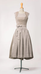 Dirndlschürze aus naturfarbenem Bio-Leinen mit eingewebtem Muster, kombiniert mit Mieder Ava in hellem Naturton und Rock Marlene in goldbraun – Frontansicht auf Büste, handgefertigt von Zirbenfux