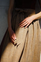 Dirndlschürze in Ocker mit Streifen aus Leinen, Nahaufnahme der Schürze am Model mit ausgeprägtem Licht- und Schattenspiel, reduziert inszeniert von Zirbenfux.