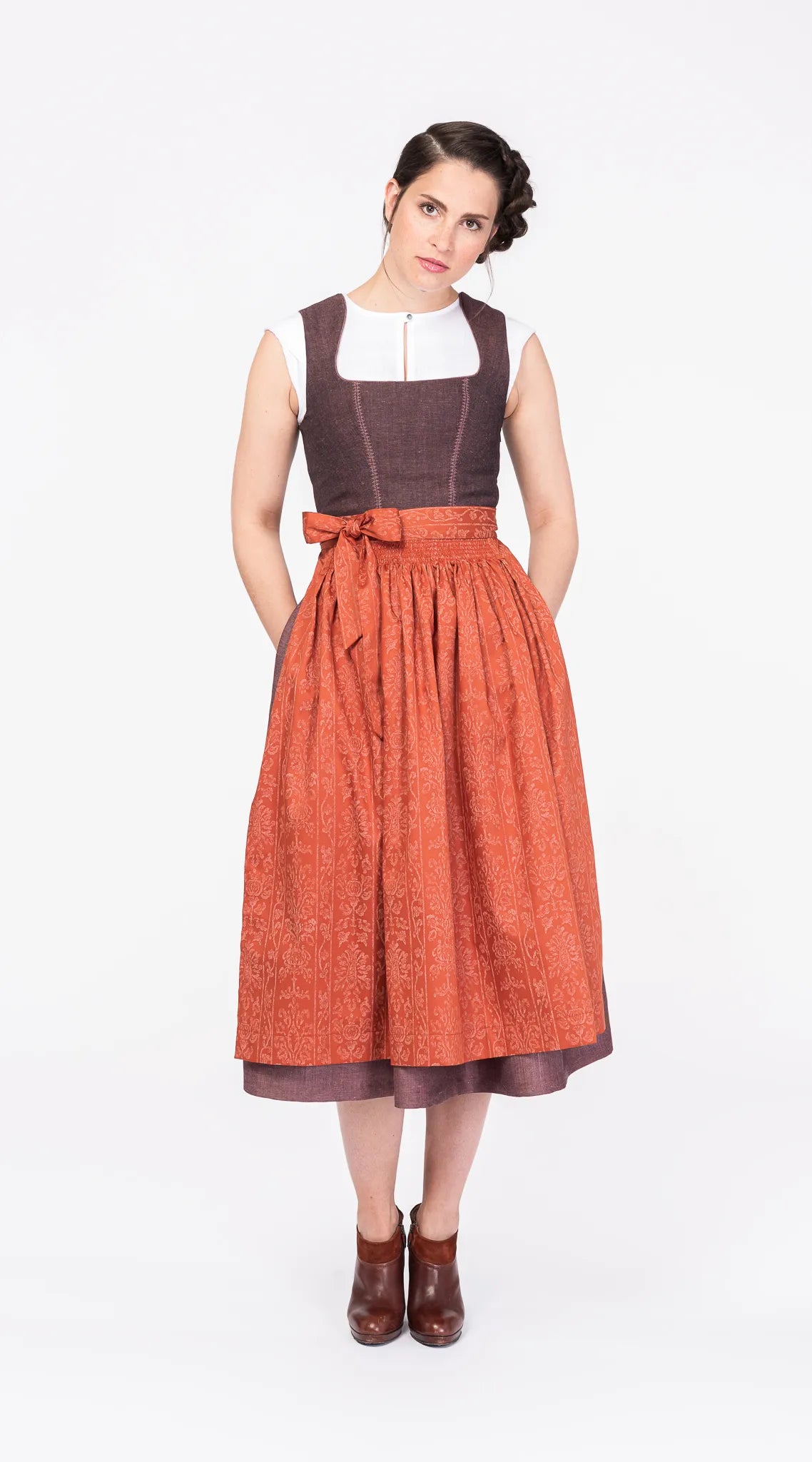 Dirndlschürze aus Baumwolle in Orange-Terrakotta – Frontansicht am Model, kombiniert mit Dirndl in Beerentönen, handgefertigt in München von Zirbenfux