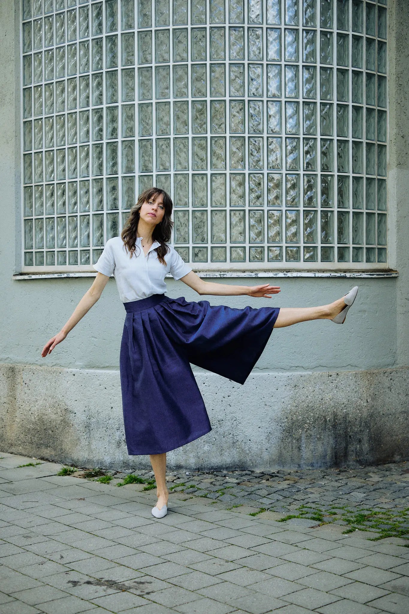 Hosenrock Audrey mit Bluse Romy im Set in Blau aus Leinen, Model in Frontansicht auf der Straße im urbanen Setting mit seitlich ausgestrecktem Bein zur Betonung des Schnitts des Hosenrocks, präzise in Szene gesetzt von Zirbenfux.