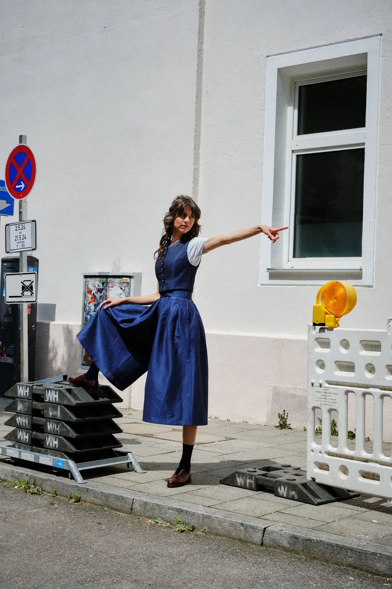 Hosenrock Audrey mit Fuxerl Charlie im Set in Dunkelblau aus Leinen, Model im urbanen Setting, ein Bein auf Baustellenelementen abgestellt und mit ausgestrecktem Arm nach hinten zeigend, markant inszeniert von Zirbenfux.