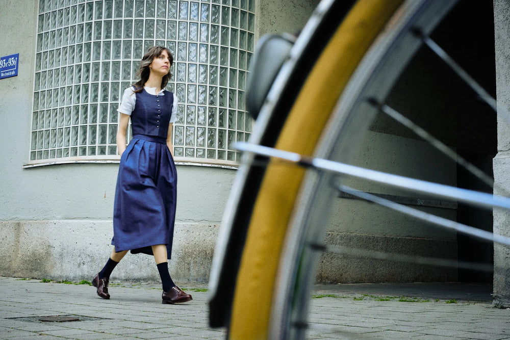 Hosenrock Audrey mit Fuxerl Charlie im Set in Dunkelblau aus Leinen, Model läuft einen Gehweg entlang in urbaner Szene, Fahrrad im Anschnitt im Vordergrund, zeitgemäß inszeniert von Zirbenfux.