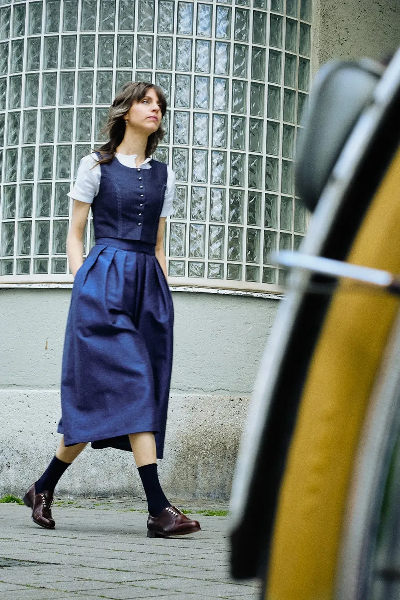 Hosenrock Audrey mit Fuxerl Charlie im Set in Dunkelblau aus Leinen, Model läuft einen Gehweg entlang in urbaner Szene, Fahrrad im Anschnitt im Vordergrund, zeitgemäß inszeniert von Zirbenfux.