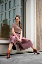 Hosenrock Audrey mit Fuxerl TILDA im Set in Malve aus Leinen, Model sitzend auf niedrigem Fenstervorsprung vor moderner urbaner Häuserfassade, Hosenrock stimmungsvoll in Szene gesetzt, klar interpretiert von Zirbenfux.