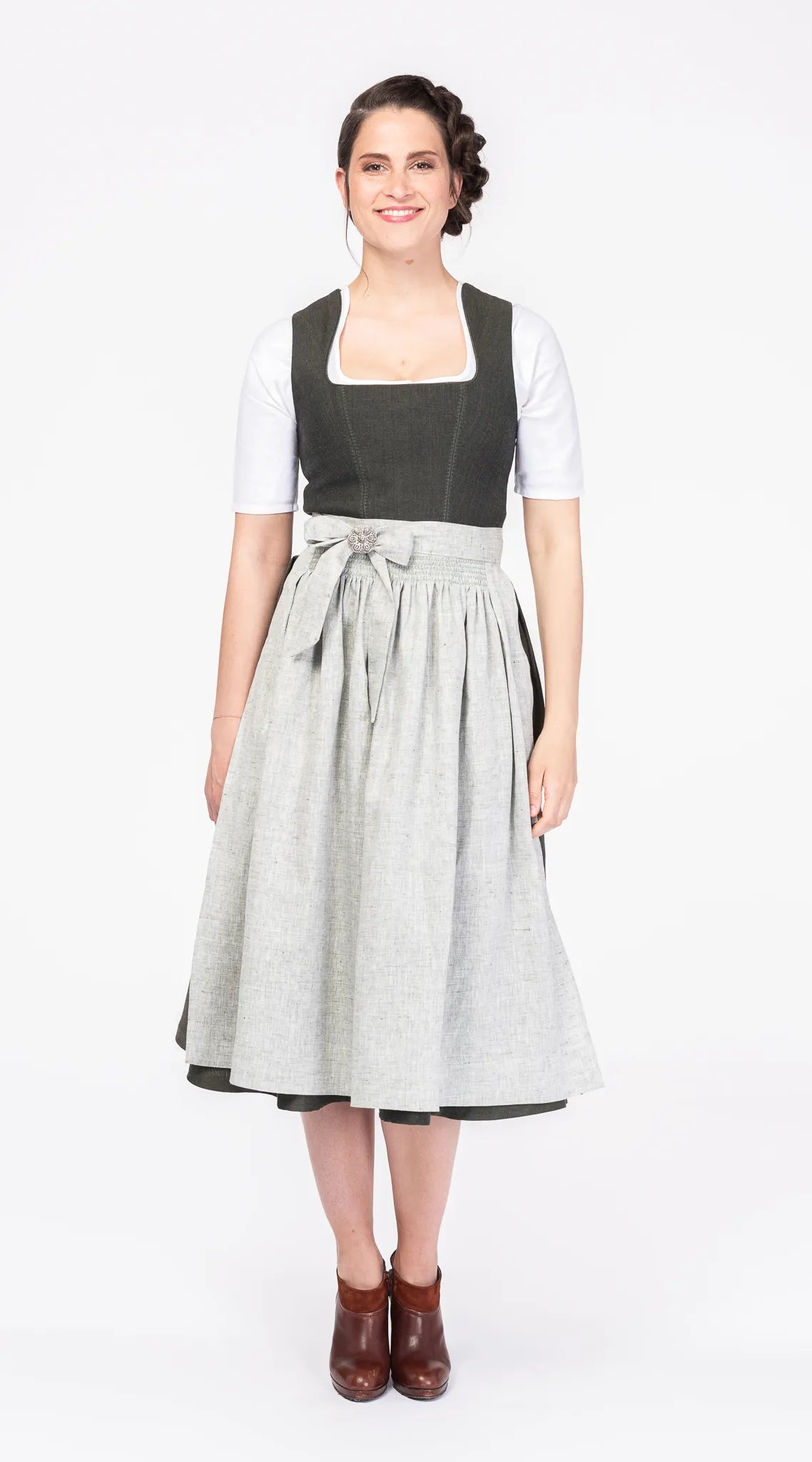 Mieder Ava aus dunkelgrüner Leinen-Schurwolle-Mischung, kombiniert mit gleichfarbigem Rock, hellgrüner Schürze und Dirndlbluse Ava in Weiß – Frontansicht am Model, handgefertigt in München von Zirbenfux