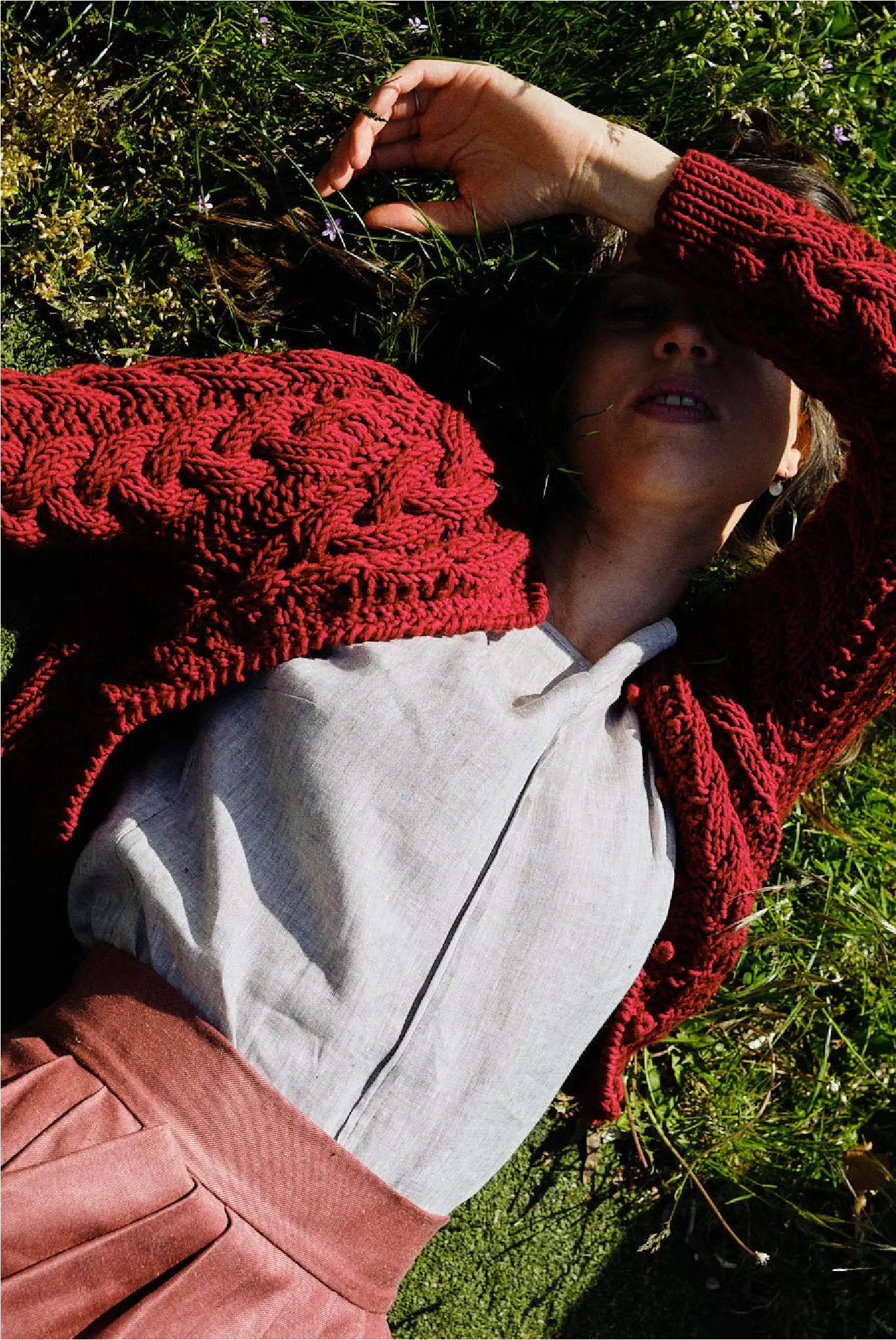 Model mit geschlossenen Augen im Gras – trägt Strickjacke Helene in Kirschrot, naturfarbene Leinenbluse Tilda und Rock in pinker Beere, handgefertigt in München von Zirbenfux