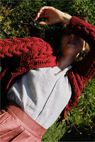 Model mit geschlossenen Augen im Gras – trägt Strickjacke Helene in Kirschrot, naturfarbene Leinenbluse Tilda und Rock in pinker Beere, handgefertigt in München von Zirbenfux