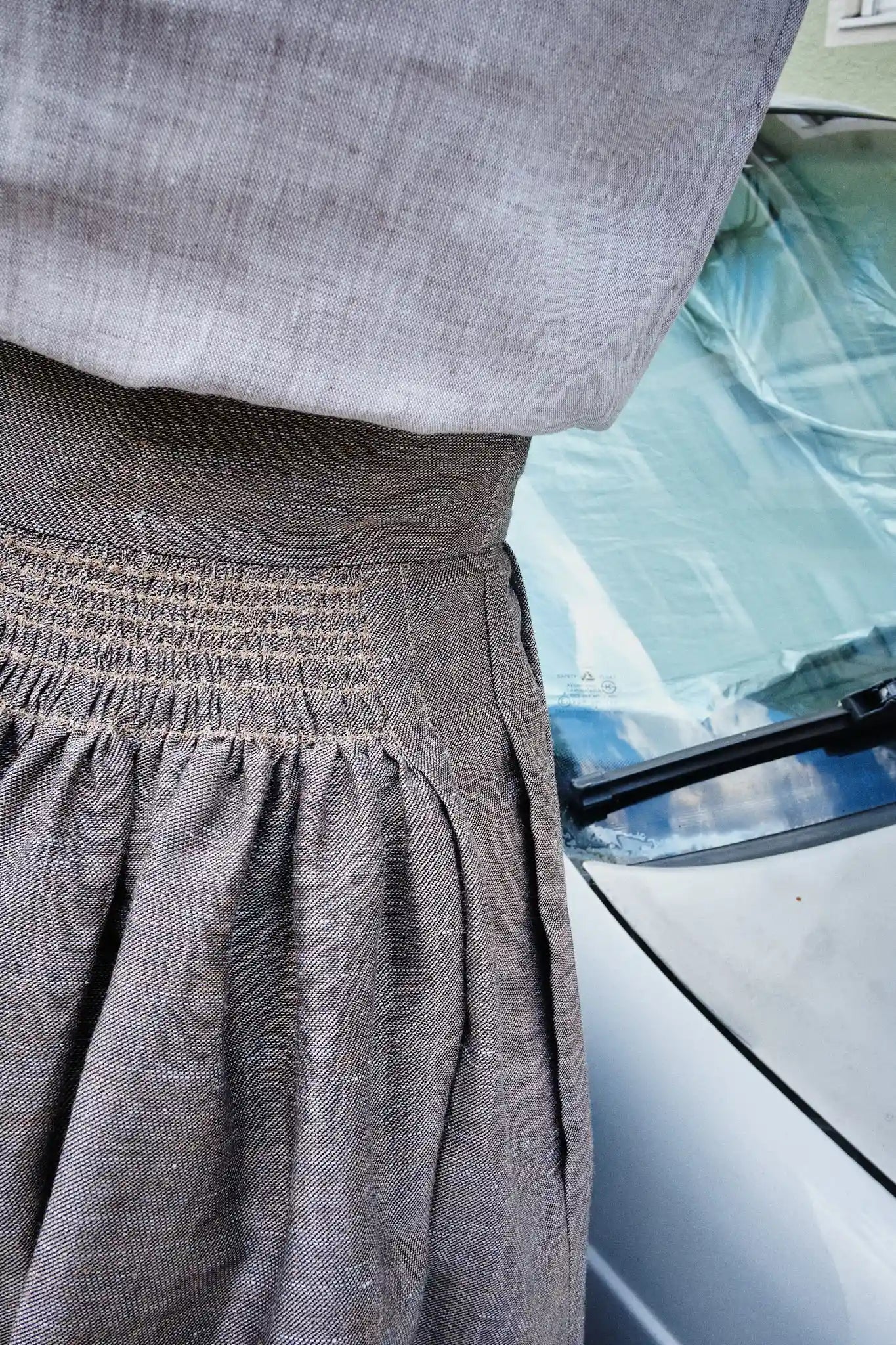 Nahaufnahme von Bluse Tilda und Trachtenrock Marlene aus natur-goldenem Leinen – Rückansicht am Model, im Hintergrund ein silbernes Auto, detailreich und urban inszeniert von Zirbenfux