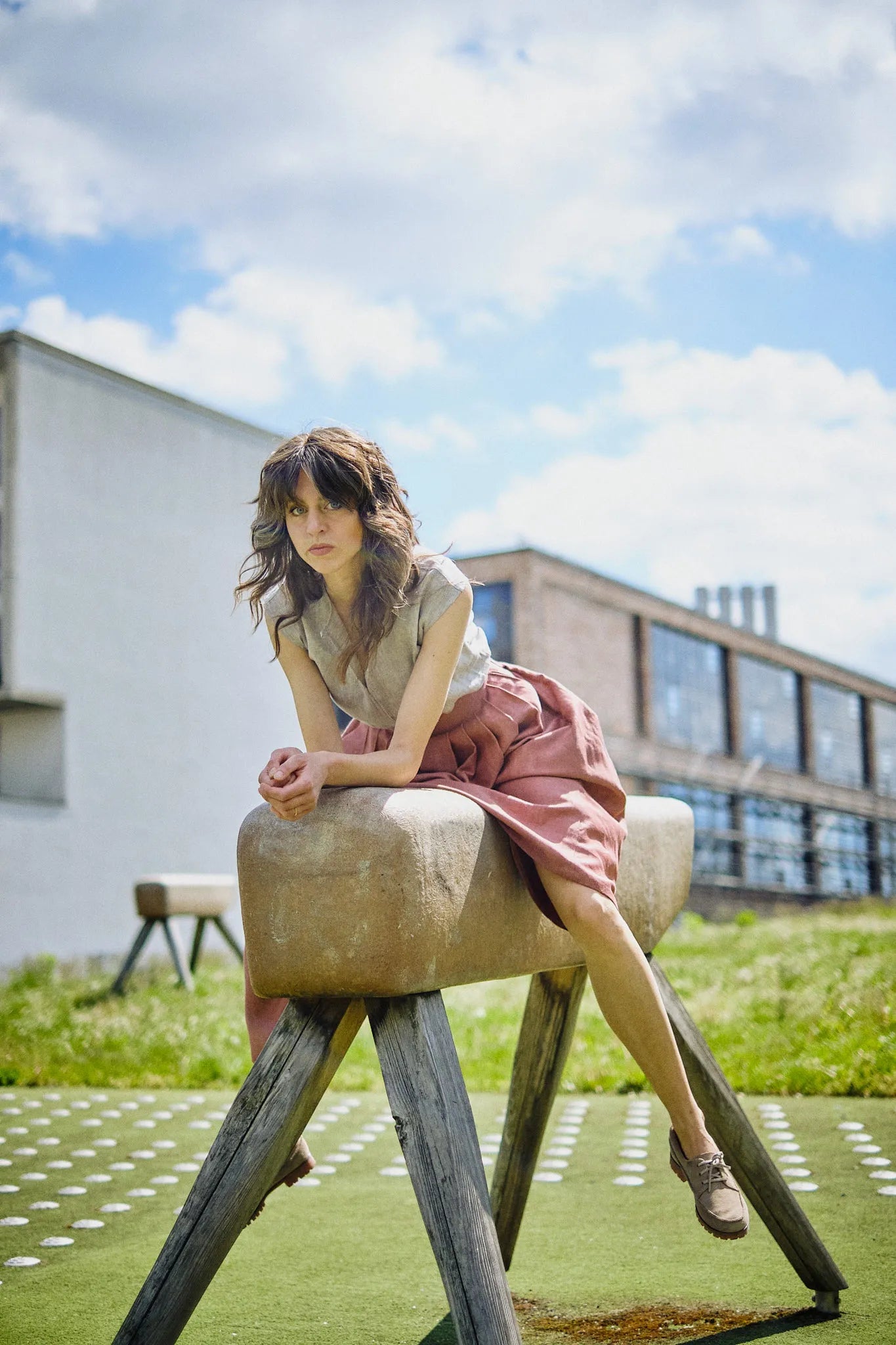 Trachtenrock Marlene in Pinke Beere mit Bluse TILDA im Set aus Leinen in Natur, Model sitzend auf einem Lederbock auf einem Spielplatz in urbaner Szene, inszeniert von Zirbenfux.