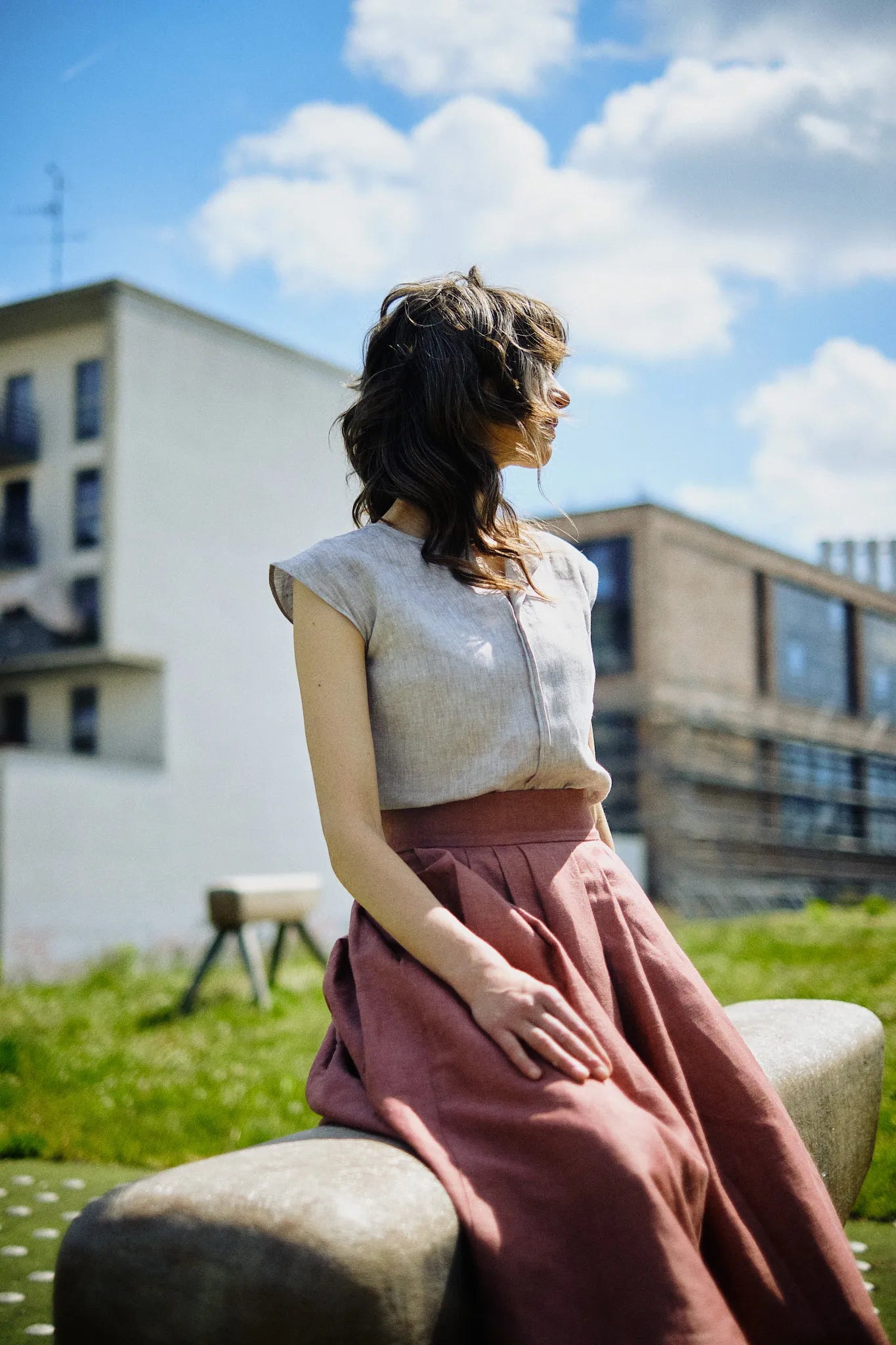 Trachtenrock Marlene in Pinke Beere mit Bluse TILDA im Set aus Leinen in Natur, Model sitzend auf einem Lederbock auf dem Spielplatz in urbanem Setting mit abgewandtem Blick, zurückgenommen inszeniert von Zirbenfux.
