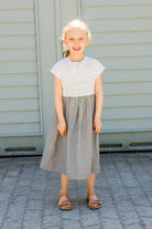 Kinderdirndl in Saphirblau – frontal vor einem Garagentor in heller Sonne stehend, fröhlich und modern inszeniert von Zirbenfüxlein