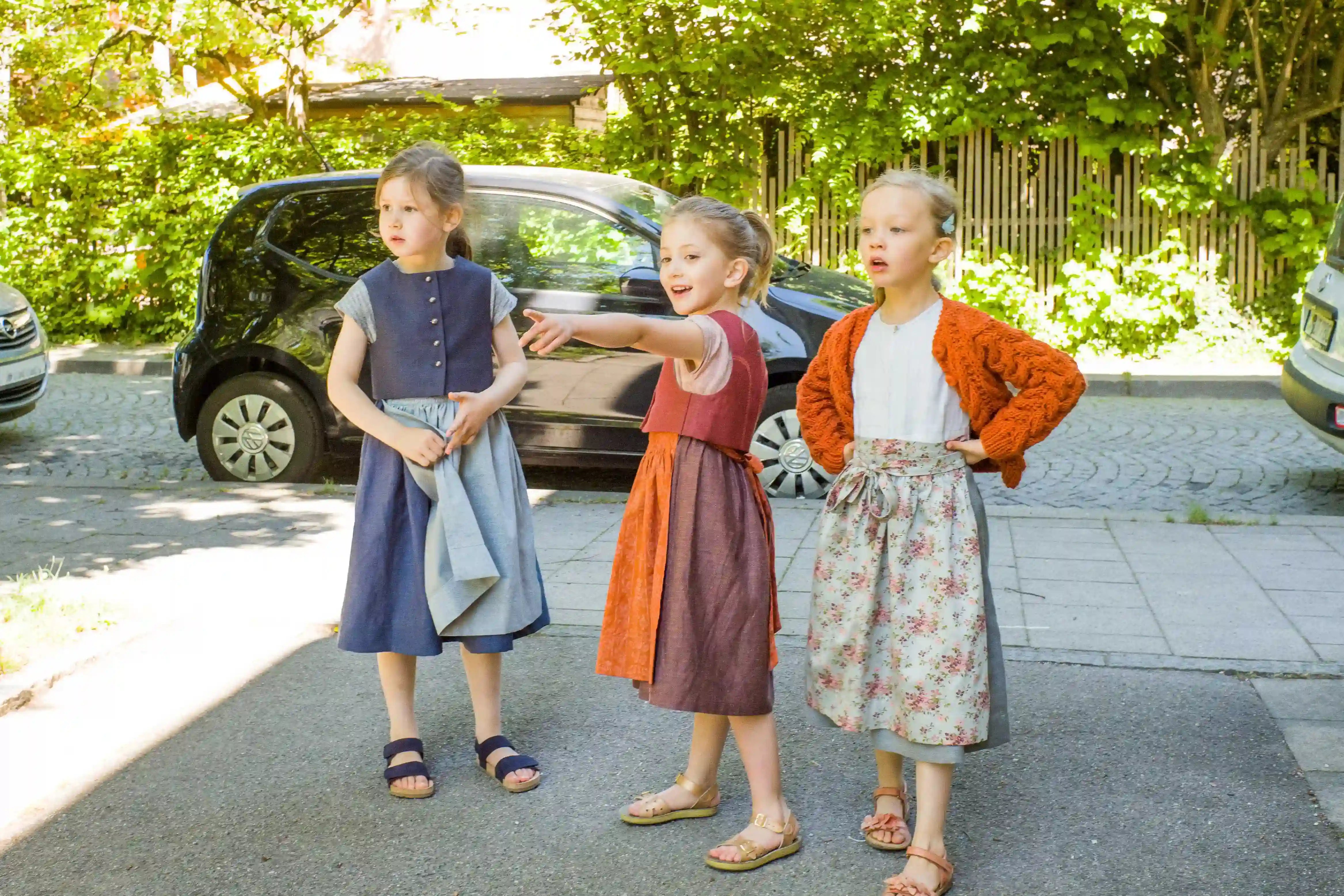 Zirbenfüxlein Kinderdirndl in Saphir, Tintenblau und pinke Beere, drei Kinder stehend in urbaner Szene miteinander beratend dargestellt, zurückhaltend inszeniert von Zirbenfüxlein.