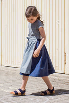 Leinen-Kinderdirndl in Tintenblau mit hellblauer Baumwollschürze – Drehbewegung nach vorne vor Garageneinfahrt, schwungvolle Szene mit Blickrichtung nach unten, lebendig interpretiert von Zirbenfüxlein