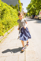 Kinderdirndl in Tintenblau mit Schürzenband – Kind läuft auf Gehweg entlang einer Straße im urbanen Setting, lebendig inszeniert von Zirbenfüxlein
