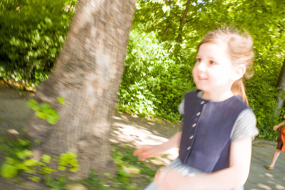 Kinderdirndl mit Weste in Tintenblau – Kind läuft lachend durchs Bild, dynamische Bewegung mit Bäumen im Hintergrund, lebendig und natürlich inszeniert von Zirbenfüxlein