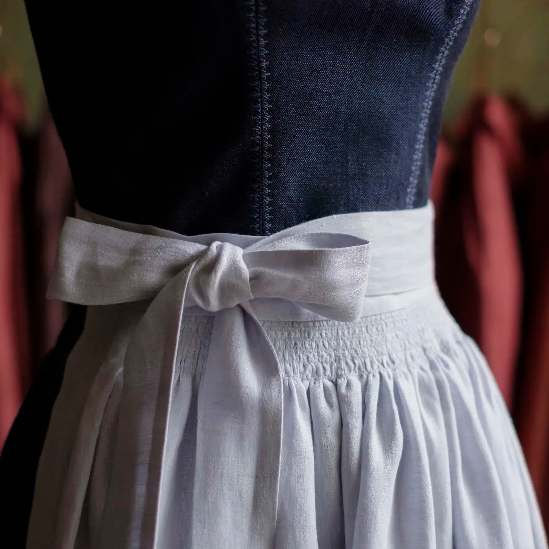 Zirbenfux Atelier München, Nahaufnahme einer gebundenen Dirndlschürze mit Mieder im Anschnitt an der Büste, handwerklich gearbeitet und konzentriert dargestellt.