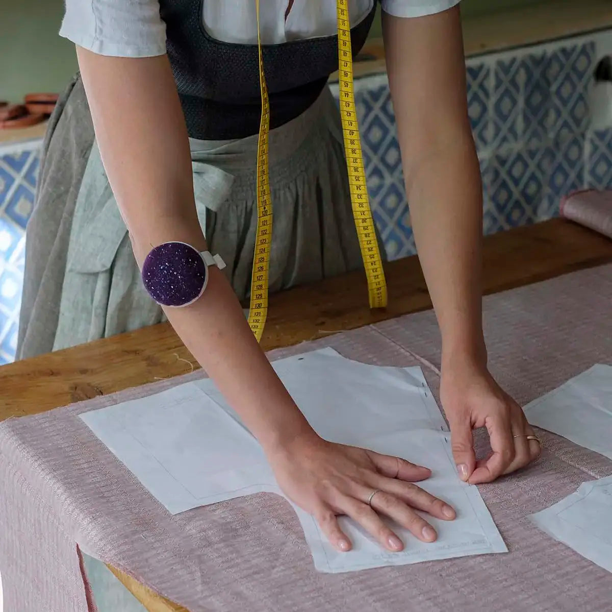 Atelierszene mit Schnitt der auf Stoff platziert wird, Oberkörper und Hände bei der Arbeit sichtbar, handwerklicher Prozess im Fokus.